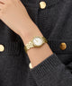 Gc Gleam Mini Small Size Metal Gold watch on a person's wrist with a dark textured sweater background