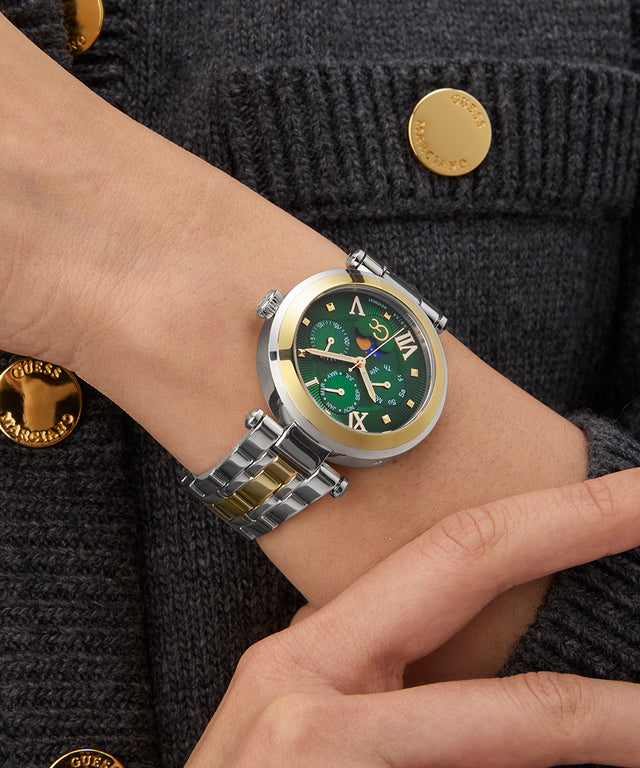 Close-up of a wrist wearing a Gc TopChic Large Size Metal watch with a green face and gold accents, against a dark textured background.