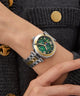 Close-up of a wrist wearing a Gc TopChic Large Size Metal watch with a green face and gold accents, against a dark textured background.