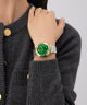 Person wearing a gold Gc Allure Mid Size Metal watch with a green face on a gray background