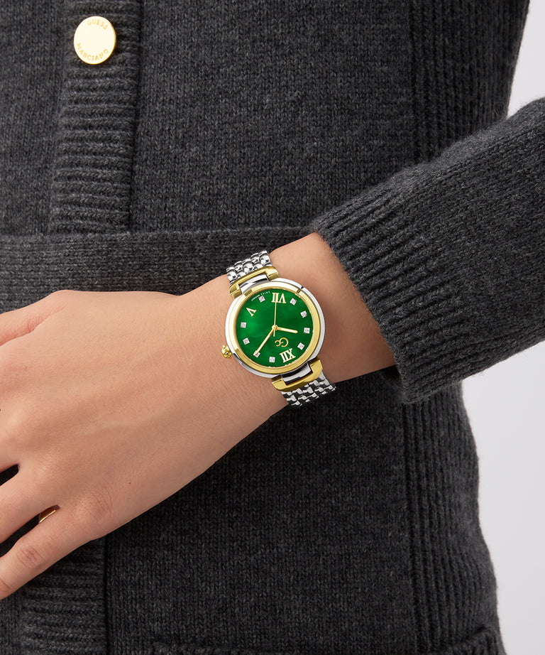 Hand wearing a Gc Allure Mid Size Metal watch with a green face and gold accents on a dark gray background