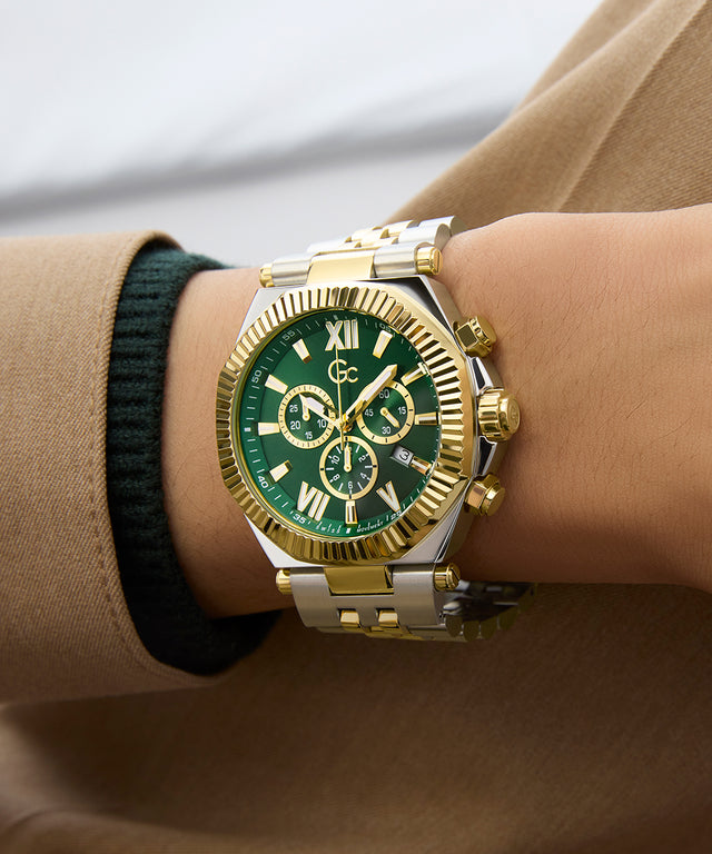 Gold and silver Gc Atlas Chrono Metal watch with green face on a wrist, wearing a beige coat.