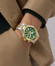 Person wearing a gold and silver Gc Atlas Chrono Metal watch with a green face on a beige coat.