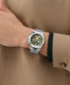 Hand wearing a Gc Atlas Chrono Metal silver watch with a green face on a brown background