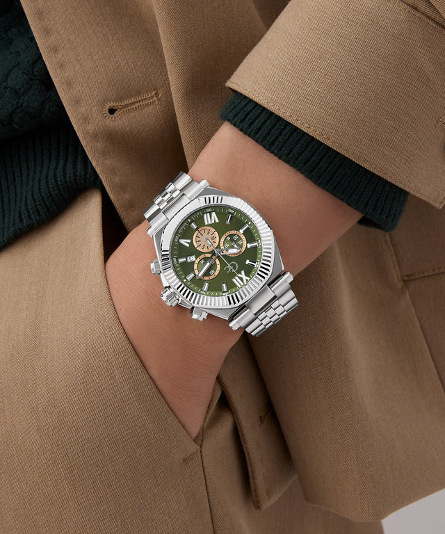 Close-up of a person wearing a silver Gc Atlas Chrono Metal watch with a green face on a brown coat.