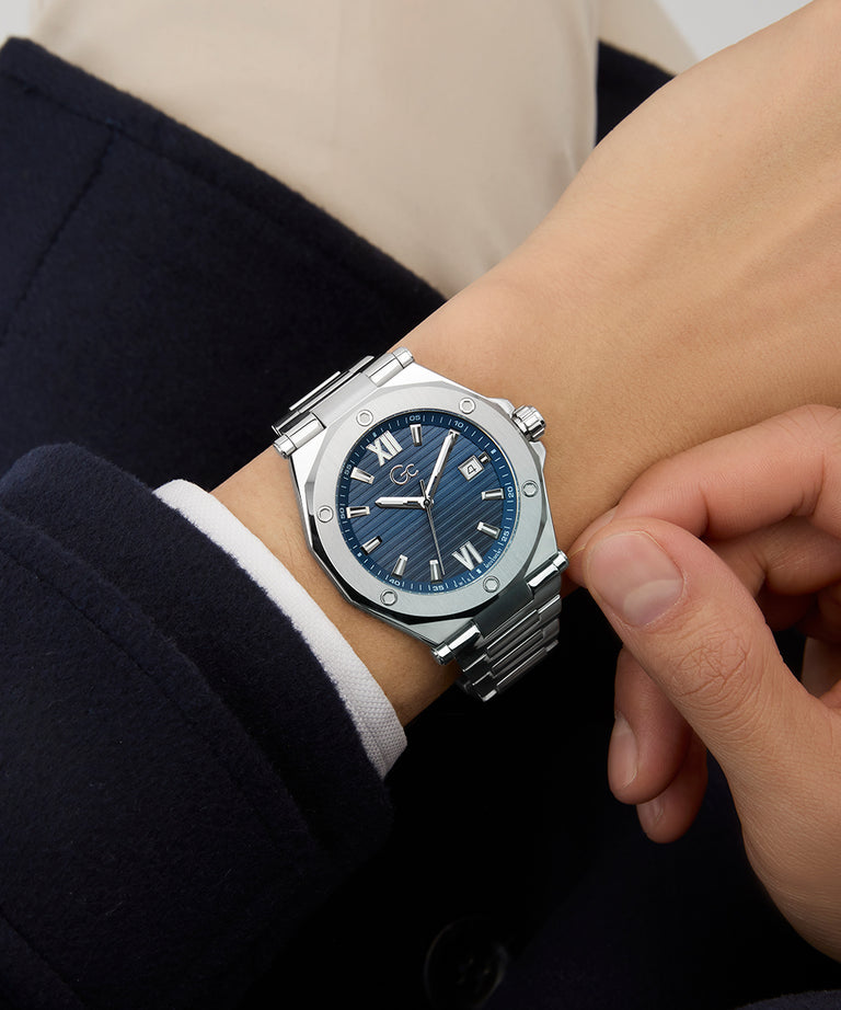 Gc Legacy Sleek Metal watch with a blue face on a person's wrist, wearing a dark coat.
