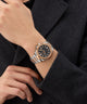 Gold and silver Gc Legacy Sleek Metal watch on a person's wrist with a dark coat background