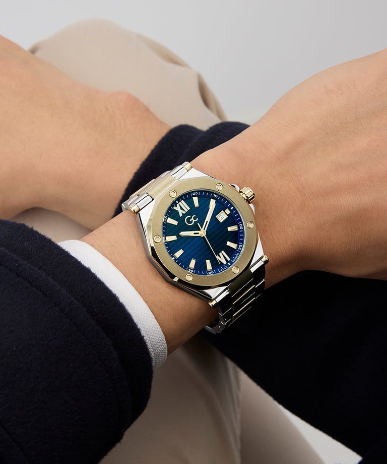 Wrist wearing a Gc Legacy Sleek Metal watch with a blue face on a neutral background