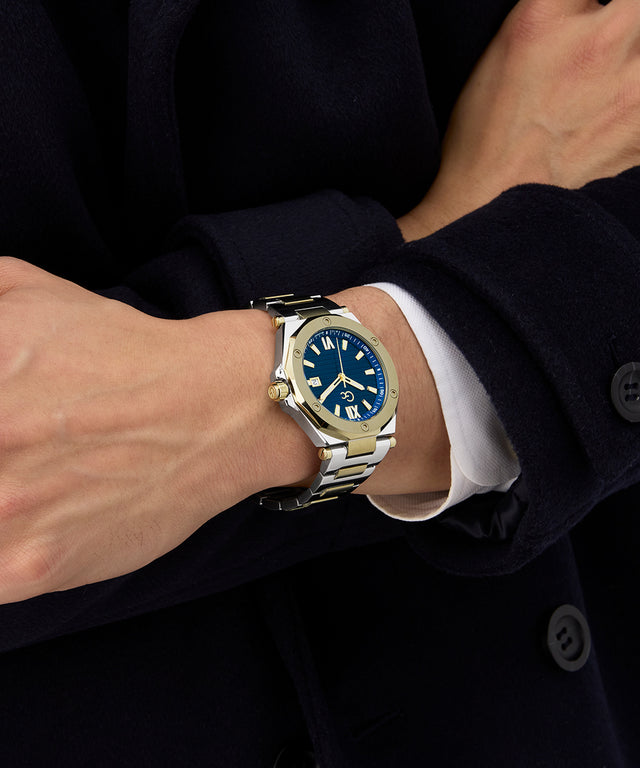 Close-up of a wrist wearing a Gc Legacy Sleek Metal watch with a blue face, against a dark background.