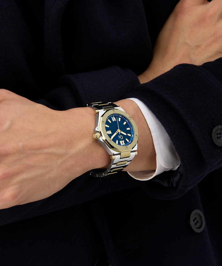 Close-up of a wrist wearing a Gc Legacy Sleek Metal watch with a blue face, against a dark background.