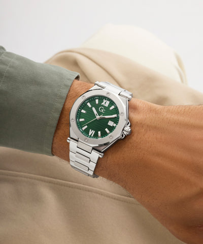 Silver Gc Legacy Sleek Metal with a green face on a wrist, wearing a beige jacket.