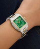 Wrist wearing a silver and gold Gc SquareCut Lady Mid Size Metal watch with a green face on a dark denim background