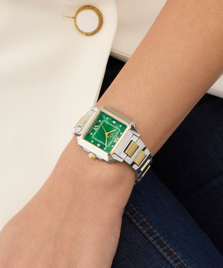 Wrist wearing a silver and gold Gc SquareCut Lady Mid Size Metal watch with a green face on a neutral background