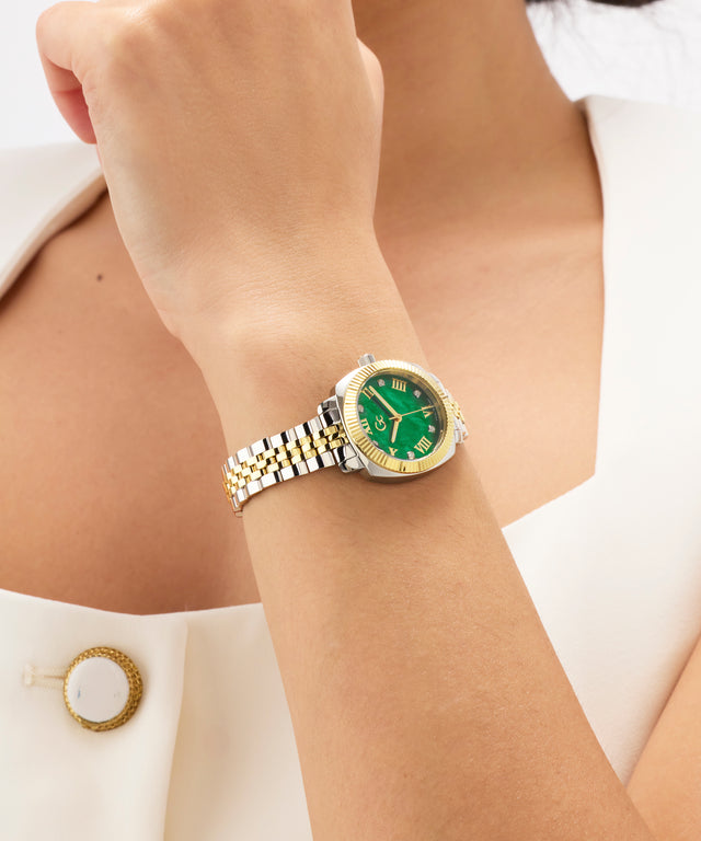 Gold and silver Gc Flair Coussin Mini Small Size Metal with green face on a wrist against a white background