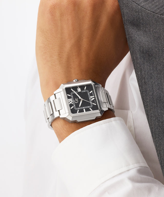 Silver Gc SquareCut Metal watch on a wrist with a white shirt and gray jacket in the background