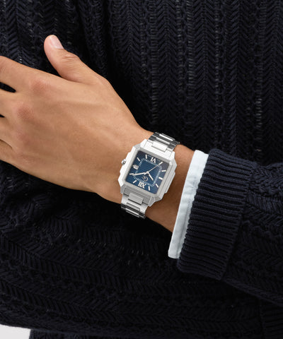 Hand wearing a silver Gc SquareCut Metal watch with a dark face against a textured black background