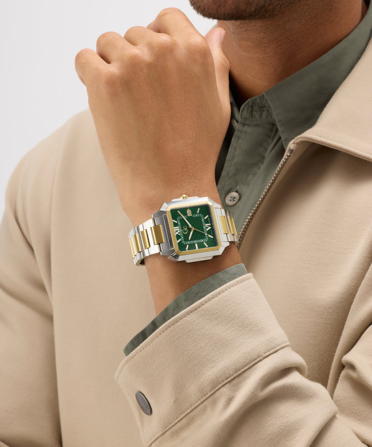Person wearing a gold and silver Gc SquareCut Metal watch with a green face on a light gray background