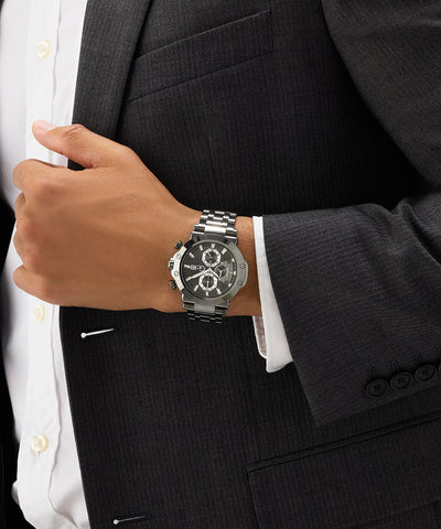 Person wearing a black suit with a silver Gc TechnoForce Chrono Metal watch on a dark background