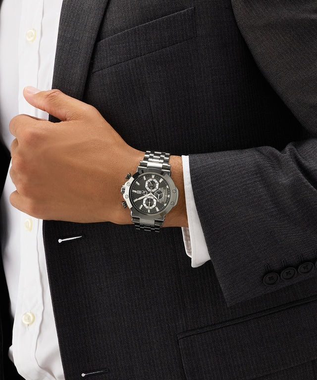 Person wearing a black suit with a silver Gc TechnoForce Chrono Metal watch on a dark background