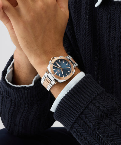 Close-up of a wrist wearing a silver Gc Nobilis Metal with a blue face, against a dark knitted sweater background.