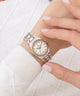 A close-up of a woman's wrist wearing a two-tone rose gold and silver watch with a white dial and crystal-encrusted bezel, paired with a white ribbed knit sweater.