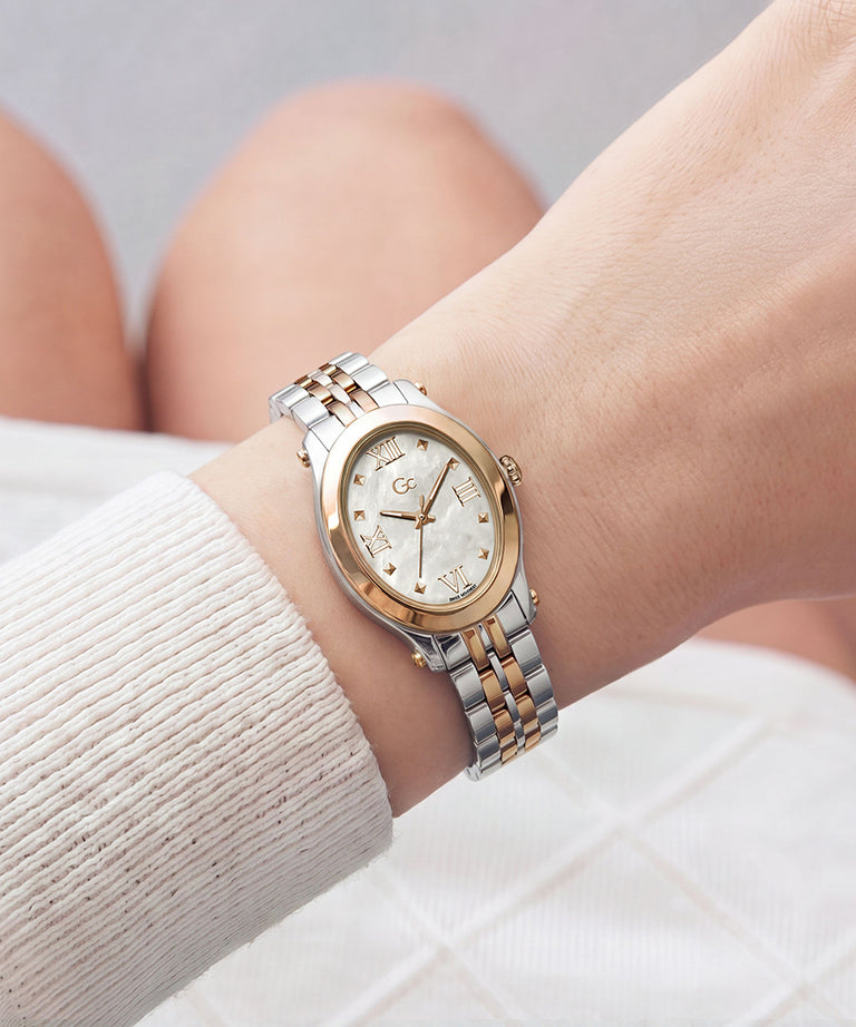 A two-tone silver and gold wristwatch with a white dial, worn on a person's wrist. The watch features a gold-tone oval case, a white mother-of-pearl style dial with gold-tone hands and markers, and a two-tone stainless steel link bracelet.